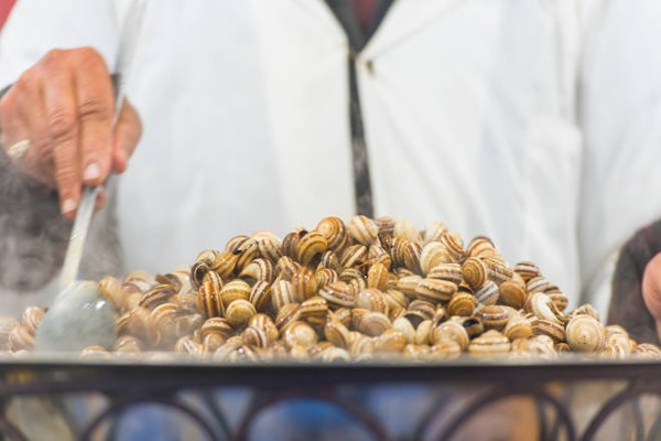 Escargots bouillis sur un marché de rue à Marrakech ou un homme cuisinant des escargots au Maroc